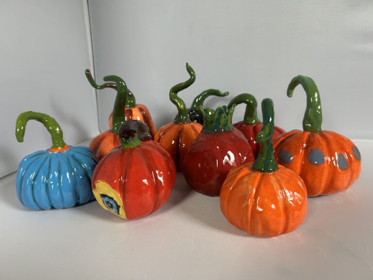 Colorful ceramic pumpkins with green stems on a white surface.