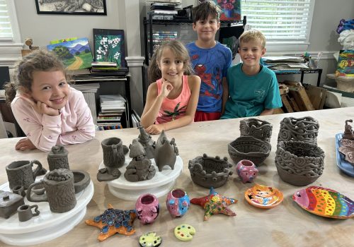 Four children proudly display their handmade pottery and clay creations.