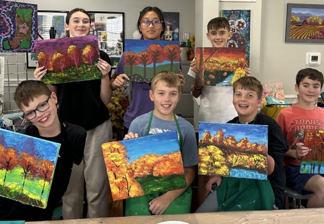 A group of children proudly holding up their colorful autumn landscape paintings.
